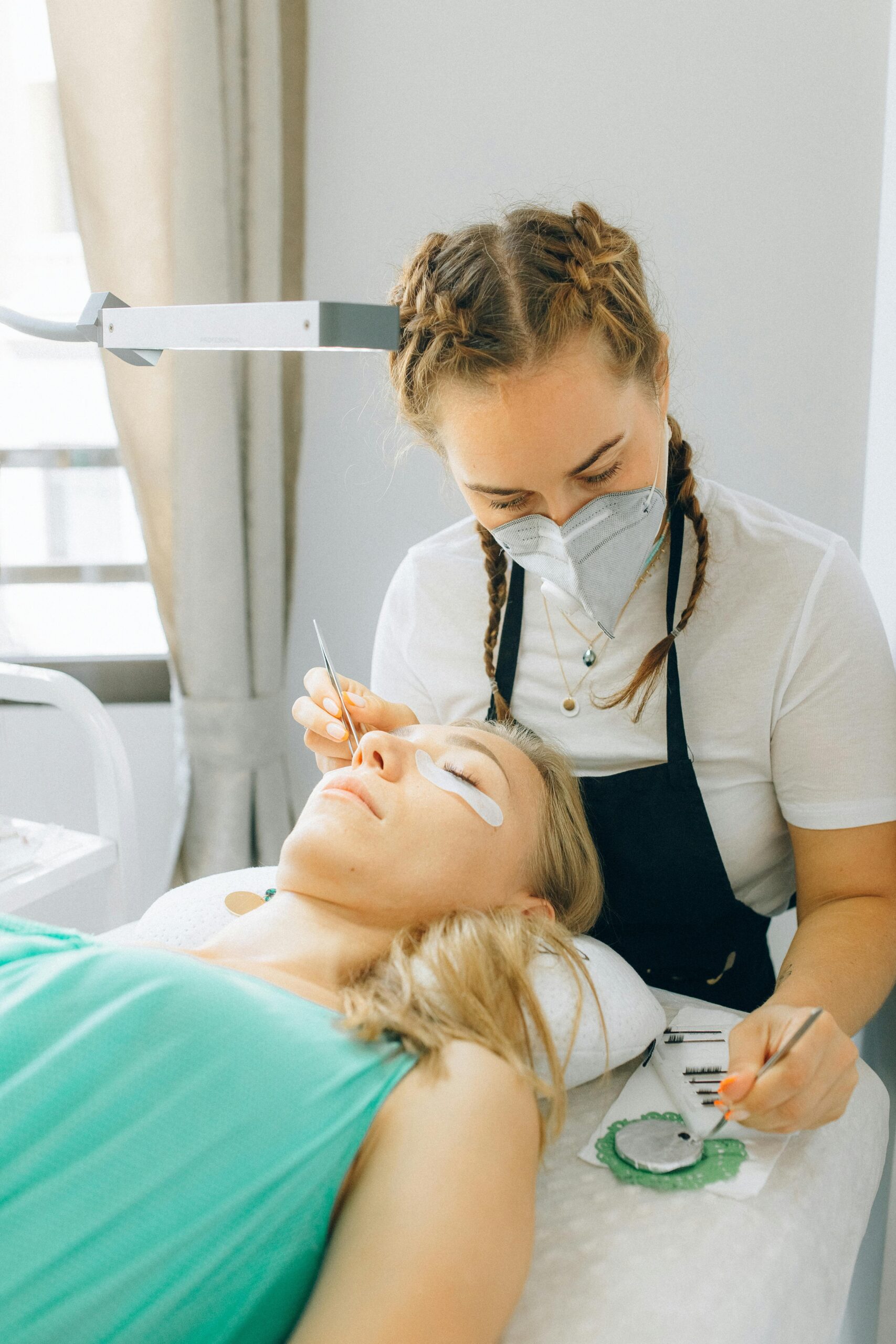 Woman receiving eyelash extension in spa setting by skilled beautician.